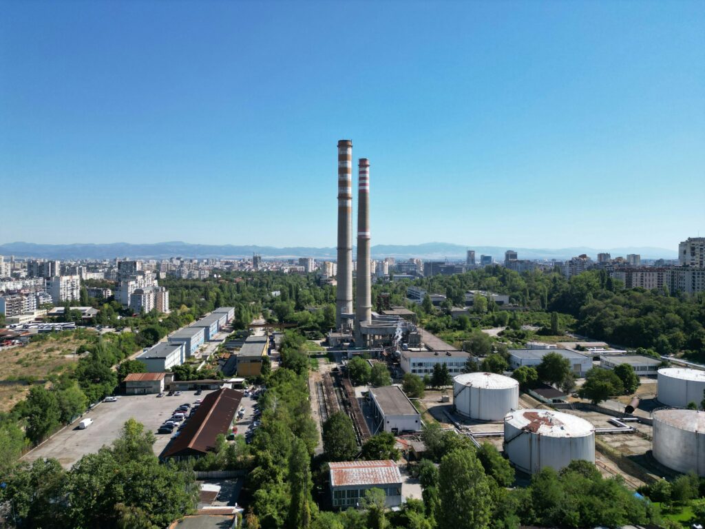 Aerial shot of an industrial site in Sofia with smokestacks, surrounded by cityscape and greenery.